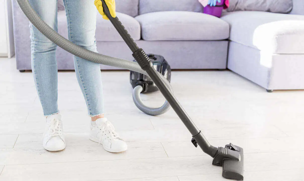 Person vacuuming near a sofa – highlighting Advantages of Surface Buffing