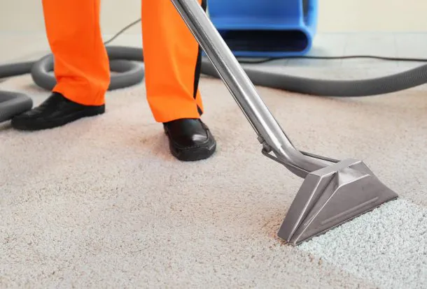 Person cleaning a carpet in a living room with a stone fireplace, using a carpet cleaner.